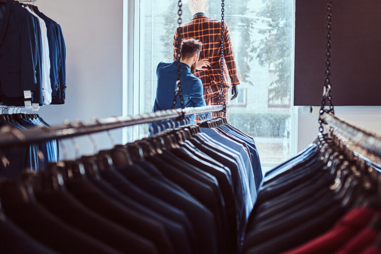 Stylish bearded seller care about suit on a mannequin in a menswear store.